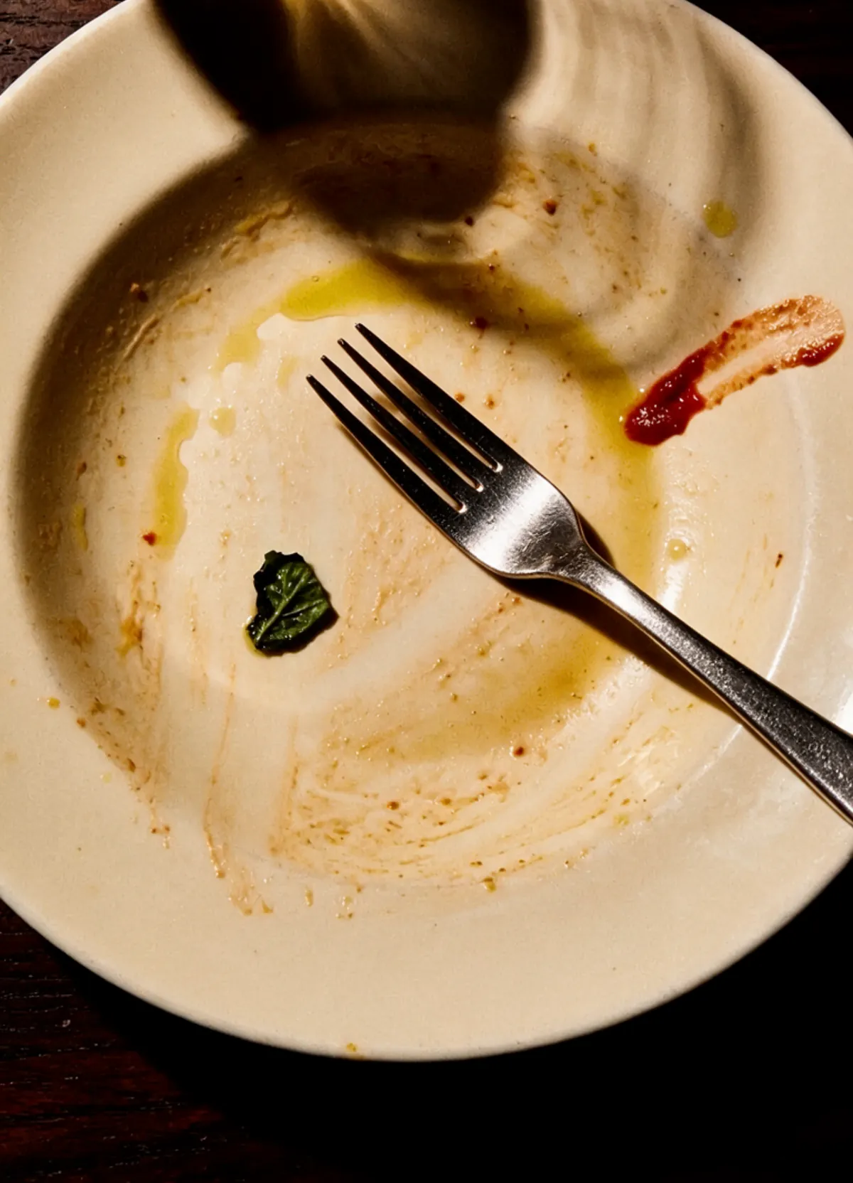 An empty plate after a meal, fork resting on it, warm flash light