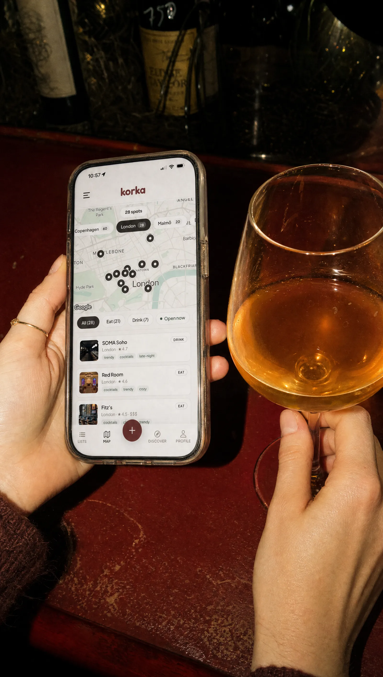 A hand holding a phone showing the Korka map, beside a glass of orange wine on a bar counter