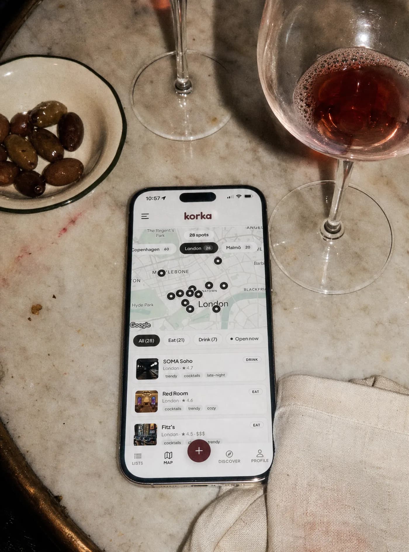 A phone on a marble bistro table showing the Korka map of London with 28 saved spots