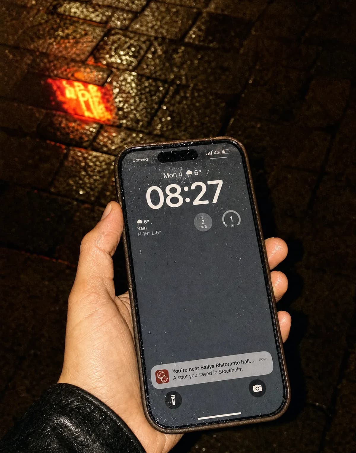 A phone on a rainy street at night showing a Korka notification about a saved spot nearby